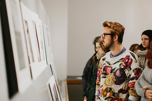 student with glasses and floral sweater examining artwork mounted to wall