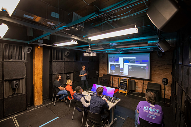 photo students and professor in immersive lab with screen on wall and speakers above and on walls