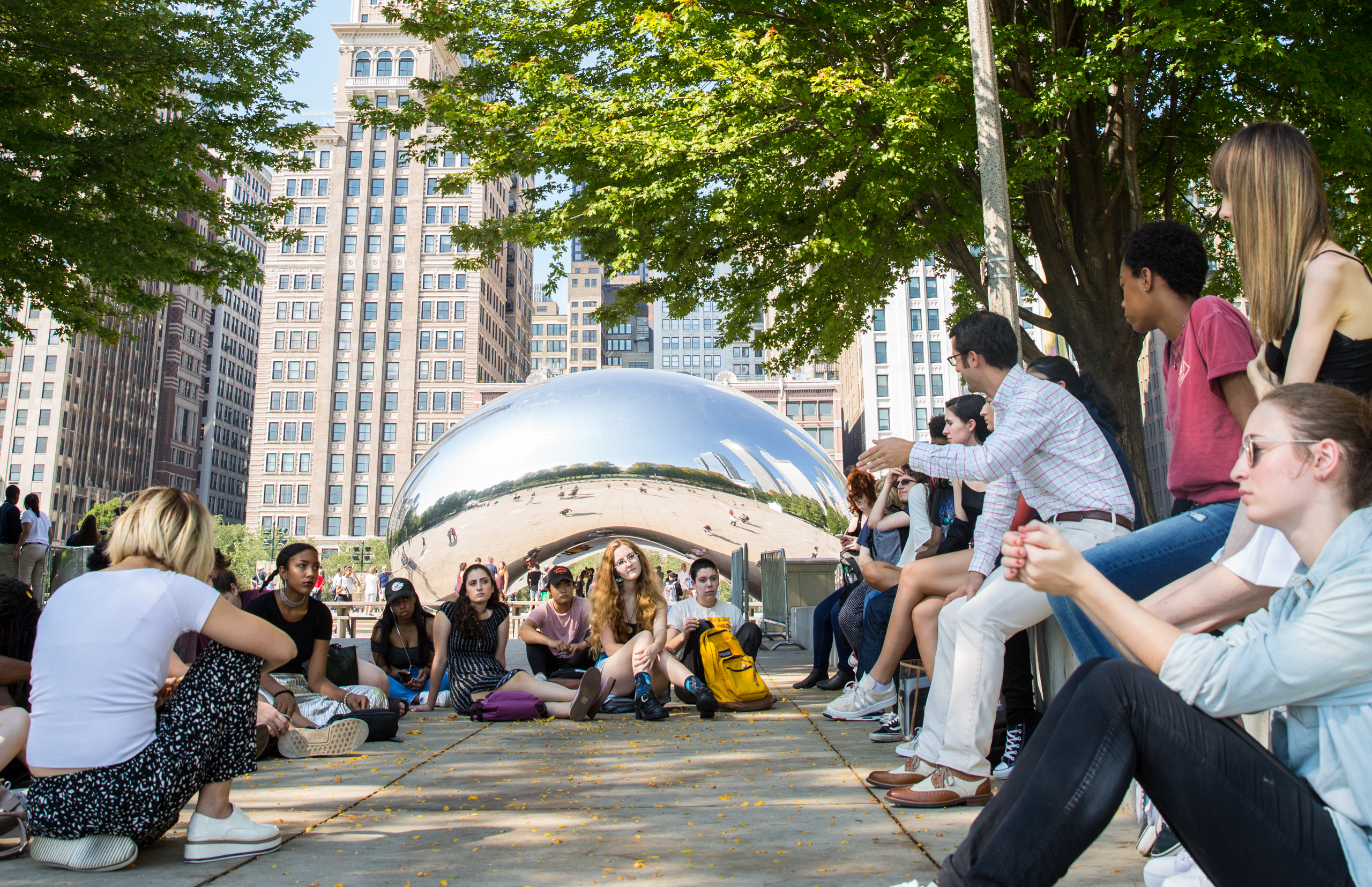 students sitting outside on a sunny day near bean shaped chrome reflective sculpture Cloud Gate in Milennnium Park
