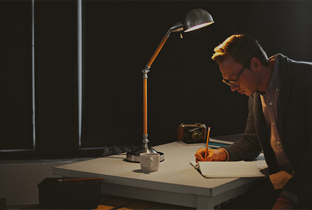 man sitting at desk sketching on paper