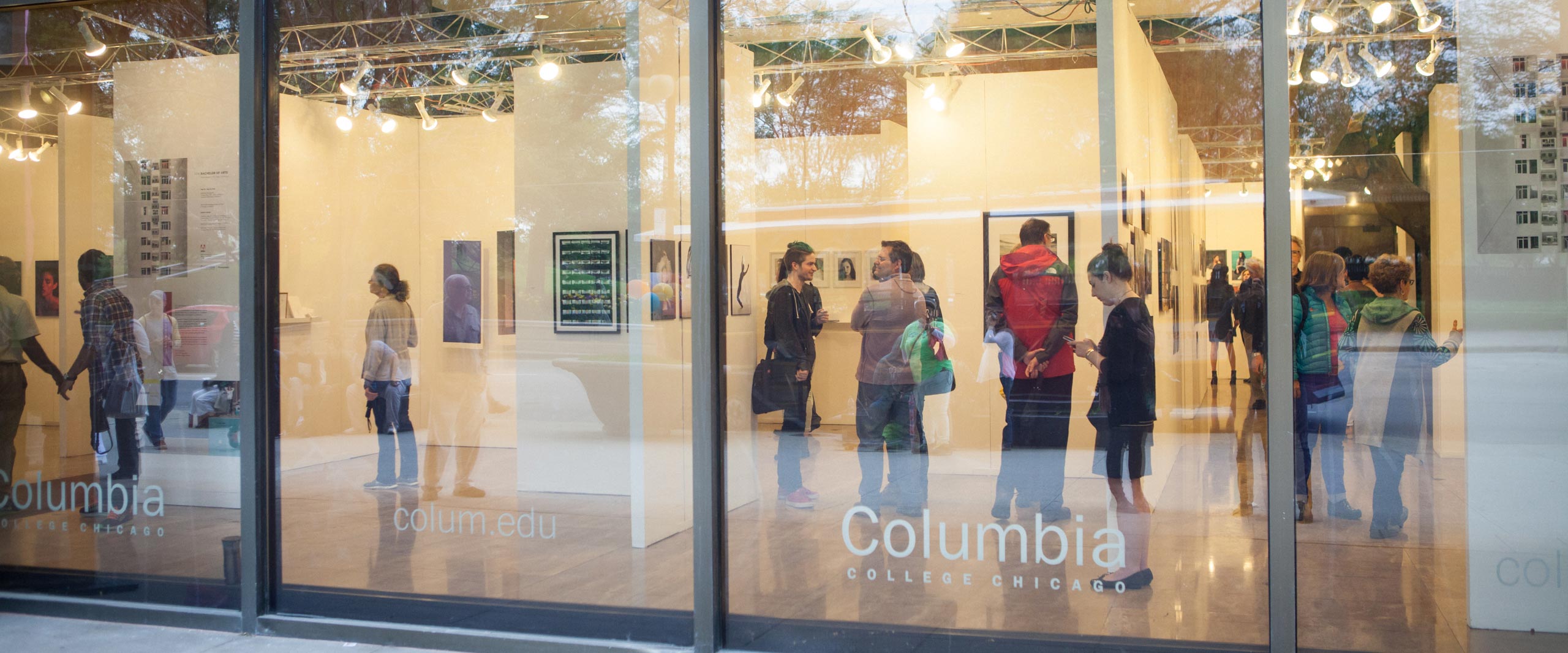 people walking around gallery viewing paintings and photographs on display