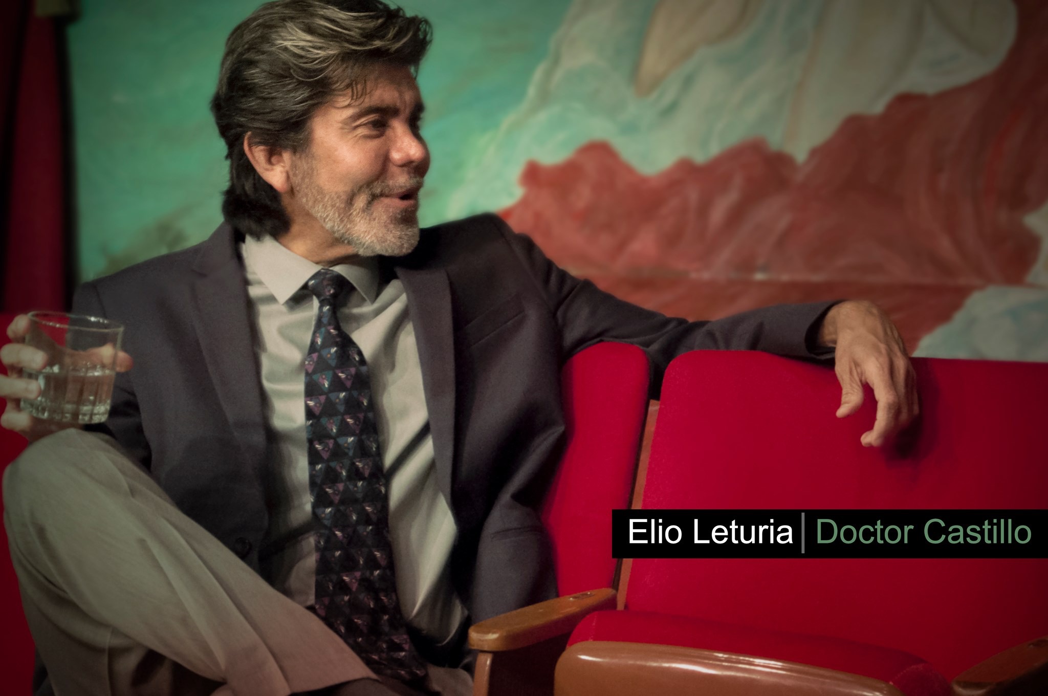 Elio Leturia sitting on a red sofa in the play Exquisita Agonía.