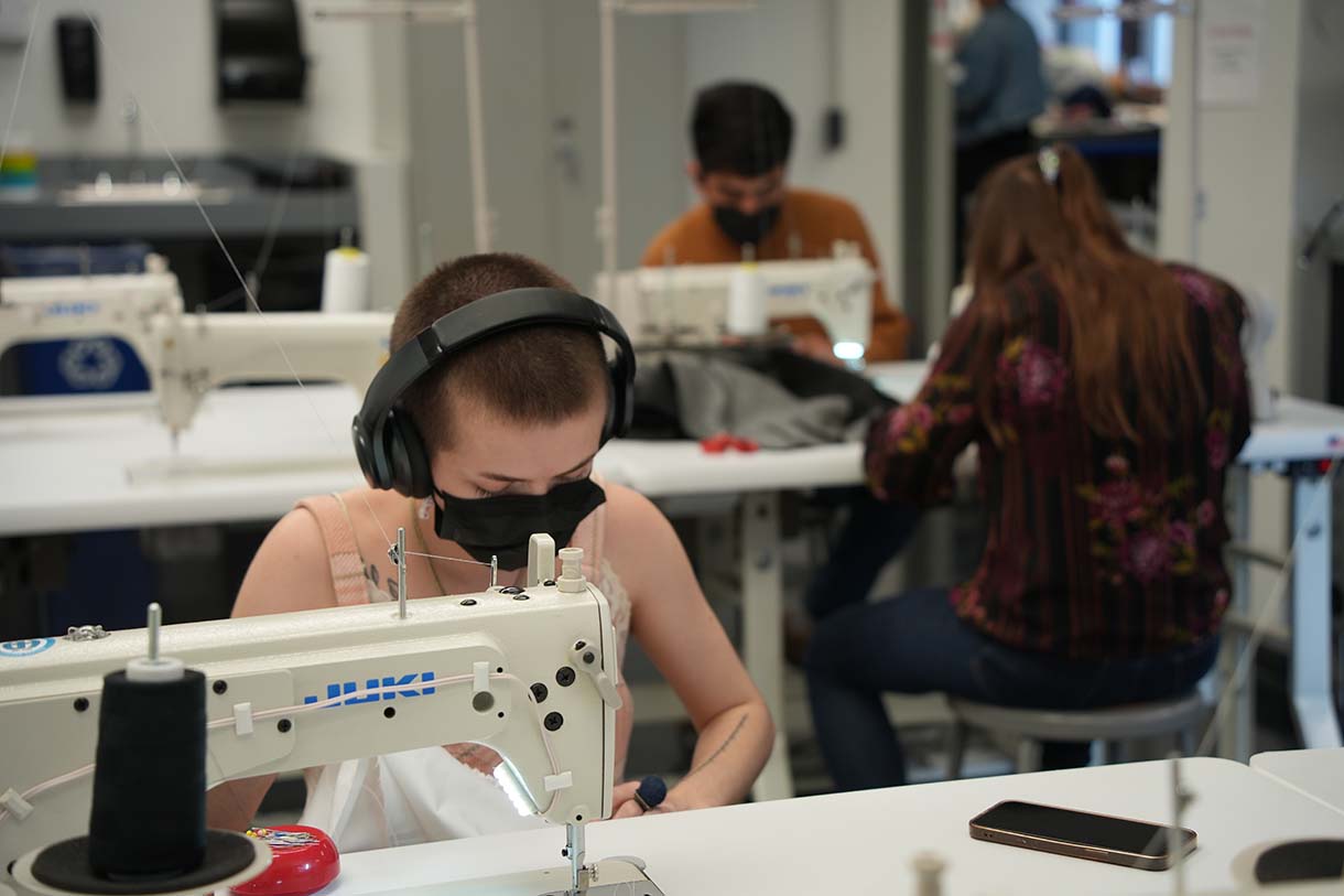 Fashion Student Ella Bondy sews at a machine with other students sewing in the background.