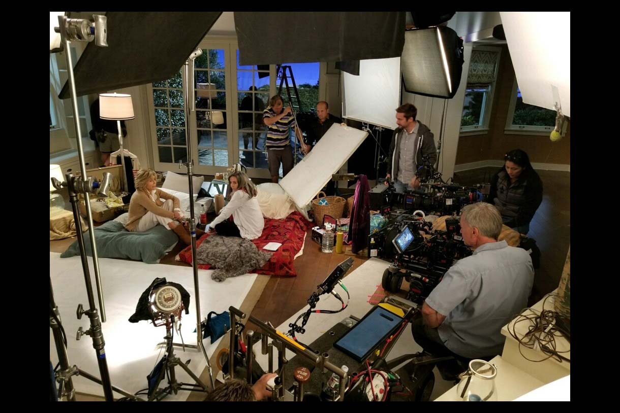 Photo of Grace and Frankie set with Jane Fonda sitting on floor surrounded by the show's crew. 