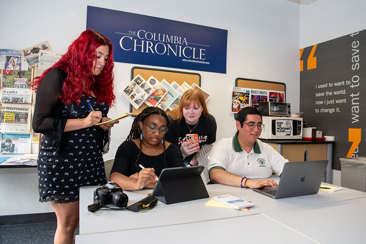 students gathered around computer with columbia chronicle signage in backgroound