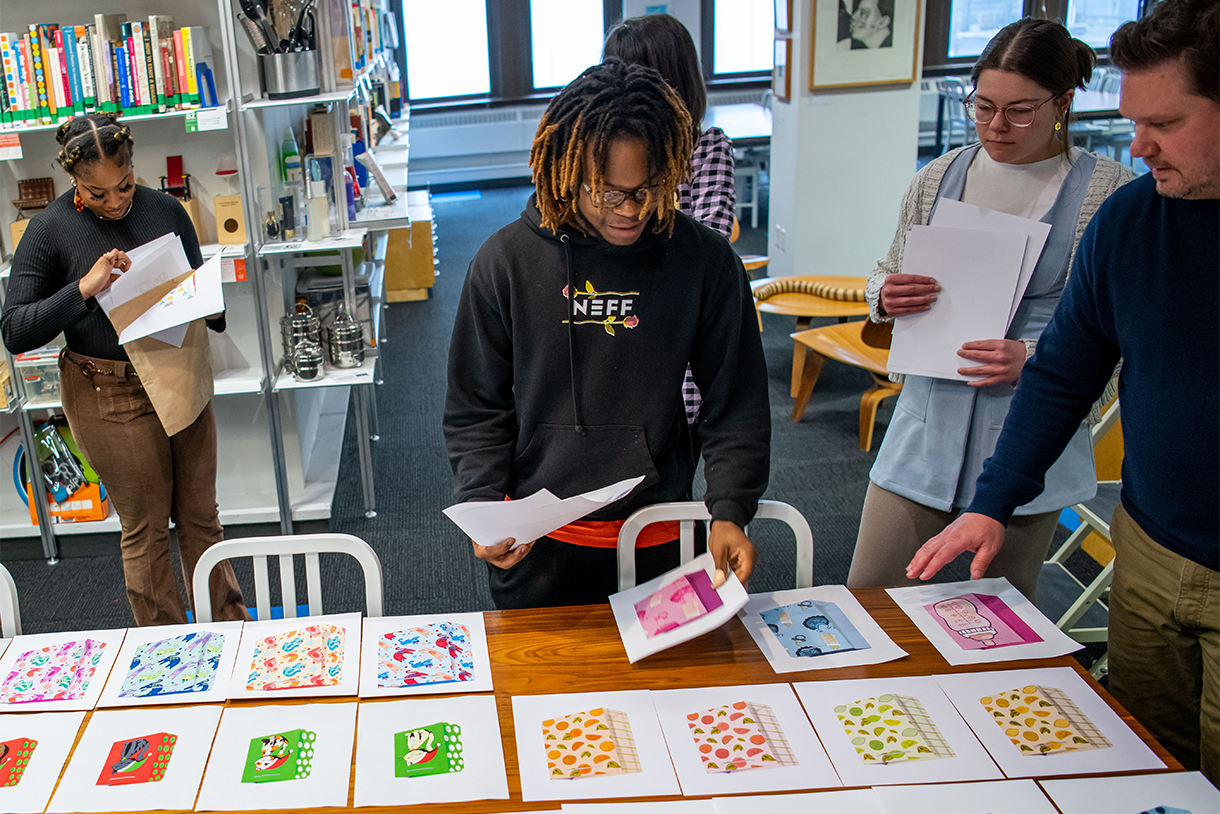 student in foreground at table arranging paper with designs on them