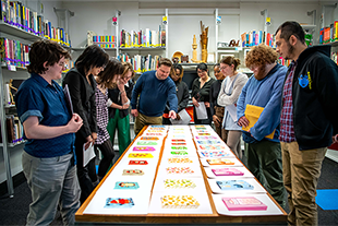 Students and professor gather around table and look at gift bag designs.