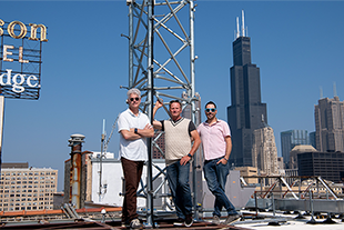 three men standing on roof with tower behind them
