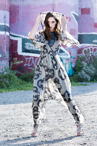 The outer layer is a jumpsuit with pleats on the waist and has covered buttons in the back. The knit layer is a jumpsuit and has the Arabic text “misconception” printed repeatedly. 